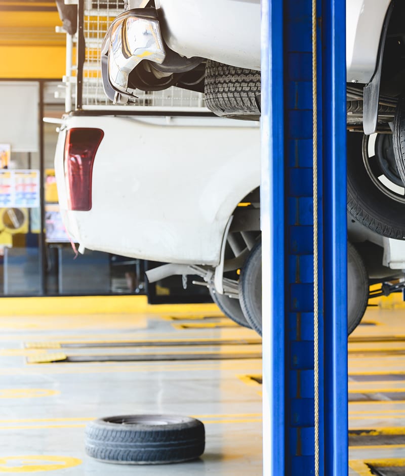 Hydra-Tech Transmissions - a white car and a white truck on lifts in an engine shop with yellow painted stripes on the wall and floor